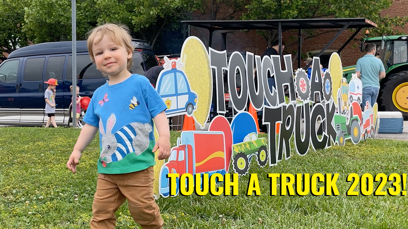 Photo of young boy standing by Touch A Truck sign